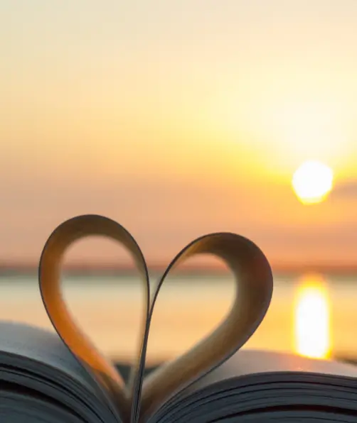 Eine Buchseite in Herzform vor einem Sonnenuntergang am Meer