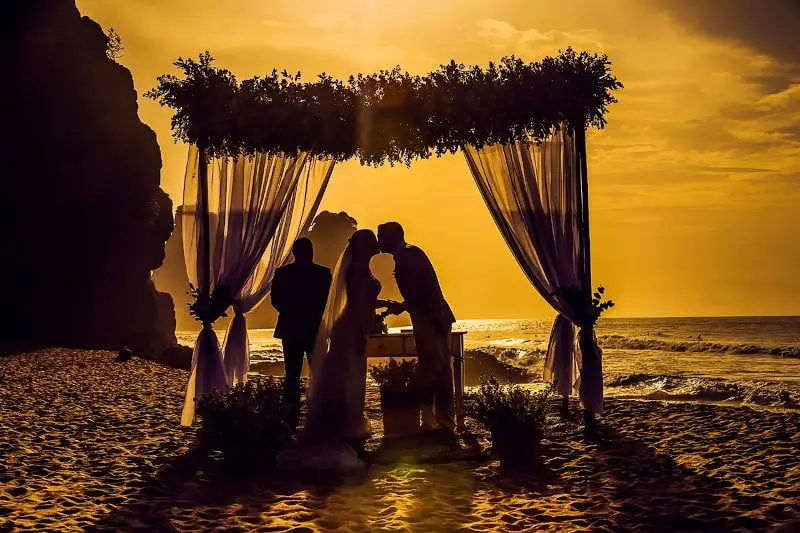 Was ist eine freie Trauung? Ein paar heiratet im Sonnenuntergang am Strand. Dieses Bild zeigt die freie Wahl des Ortes bei einer freien Trauung